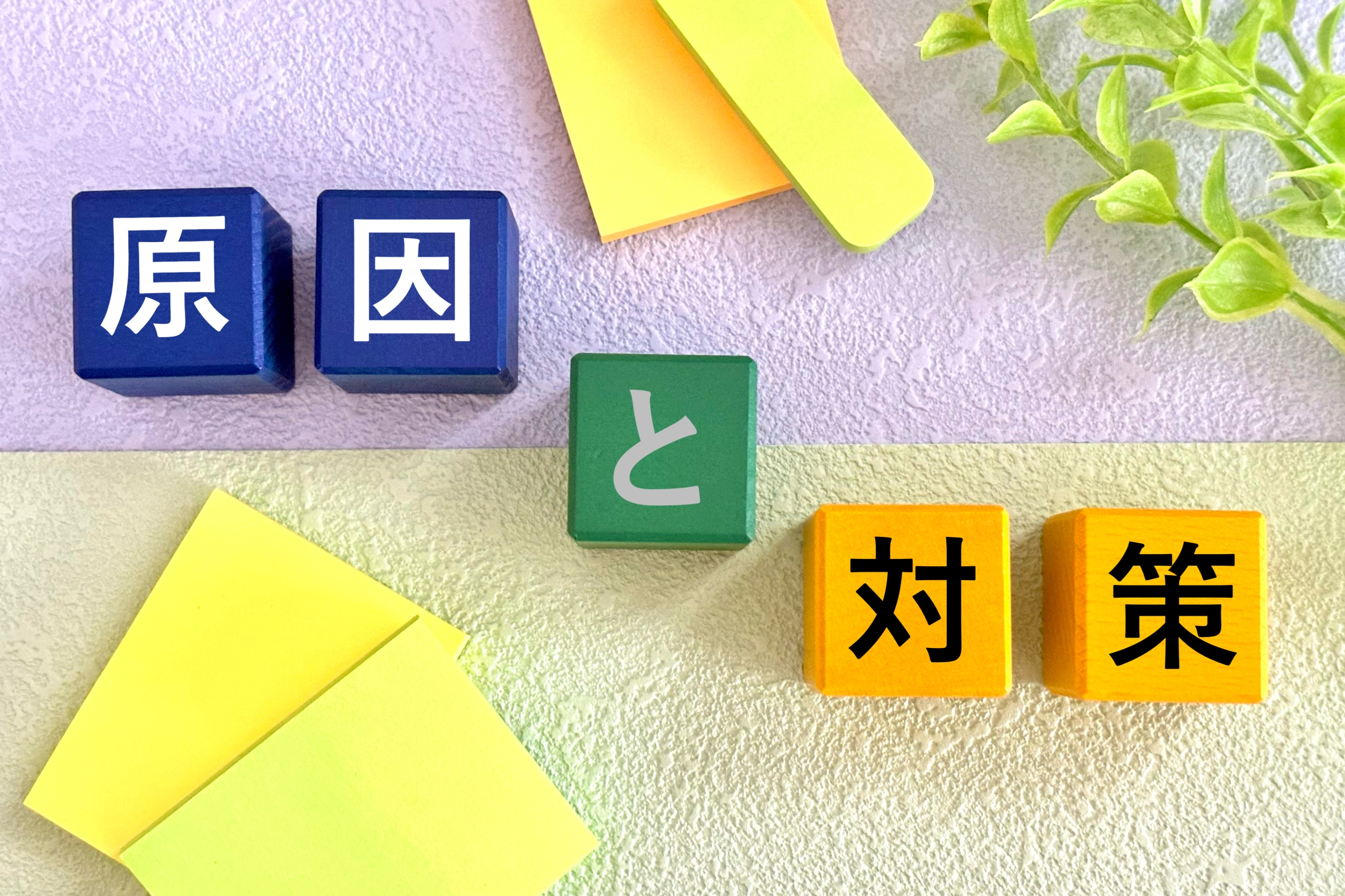 薄紫と黄緑のツートーンカラーの背景に、『原因』『と』『対策』の文字が書かれたカラフルなブロックが配置されている。左の青いブロックには『原因』、中央の緑のブロックには『と』、右のオレンジのブロックには『対策』と書かれており、周囲には黄色い付箋や緑の植物が添えられている。問題解決や分析をテーマにしたイメージ