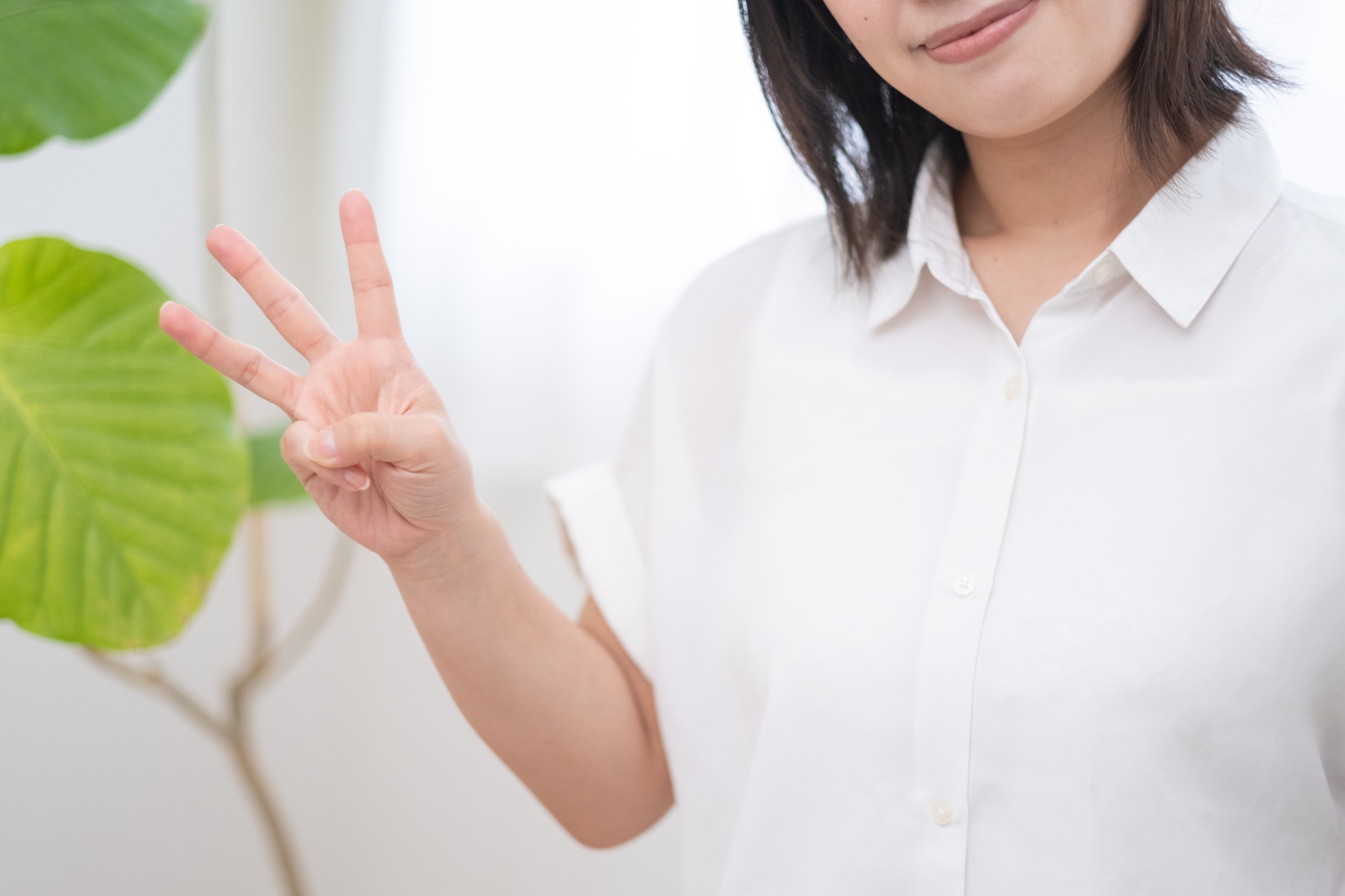 白いシャツを着た女性が、右手で指を3本立てて数字の『3』を示している様子
