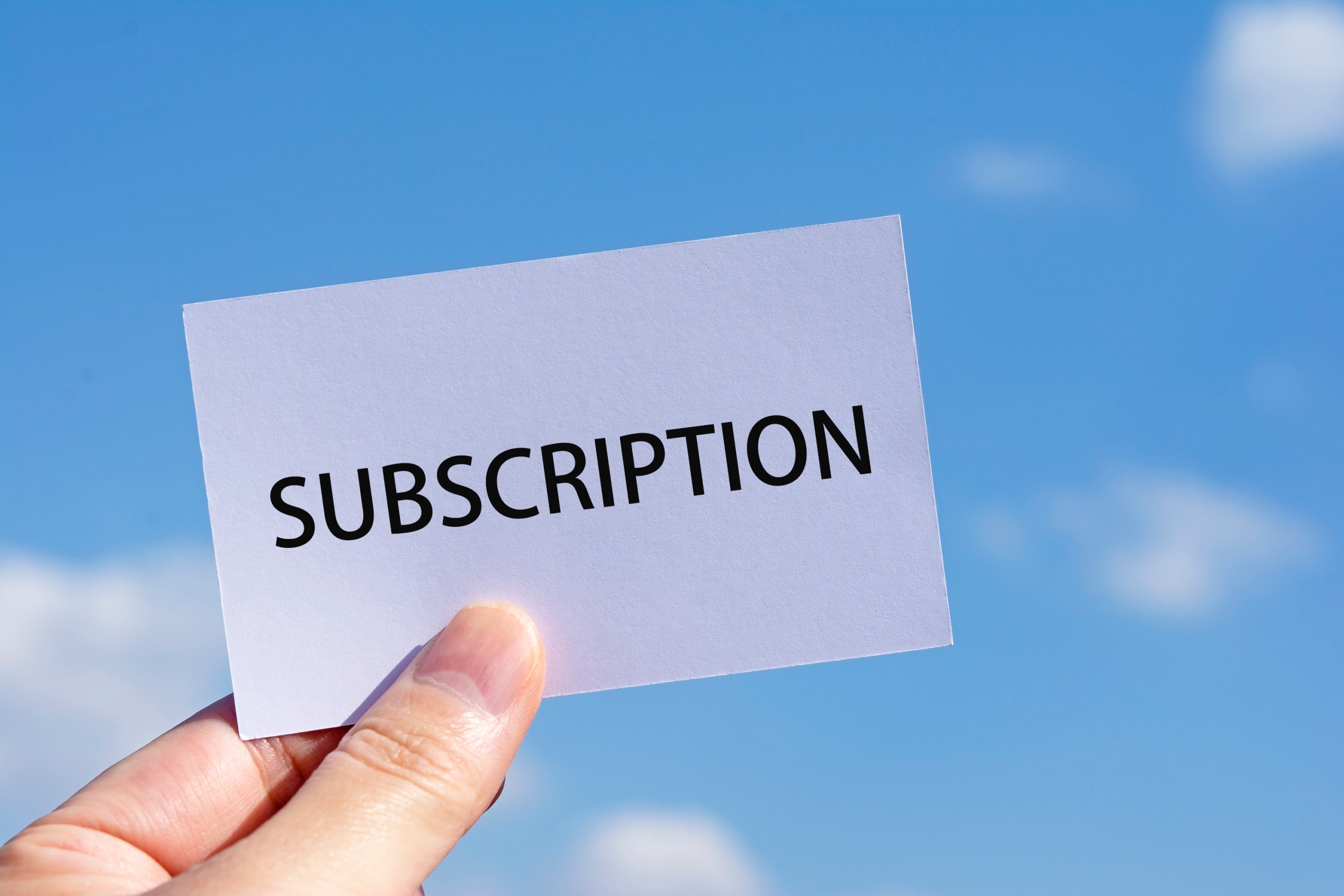 「SUBSCRIPTION」と書かれた白いカードを、青空を背景に手で掲げている様子